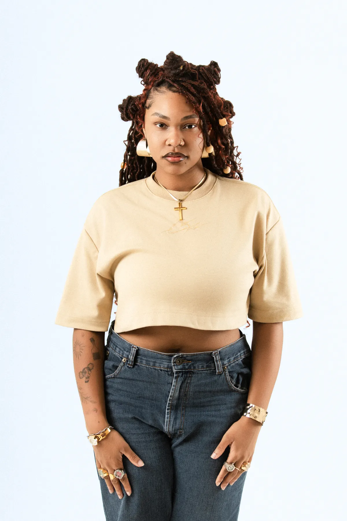 Modelo de tranças com coques, de frente, com o cropped bege e calça jeans.
